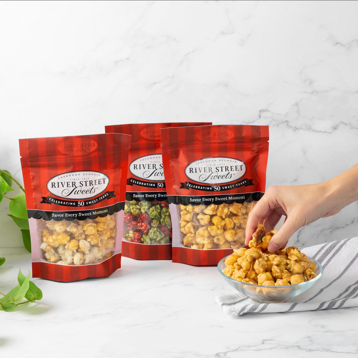 River Street Sweets bags with a hand grabbing popcorn from a bowl on a marble surface.