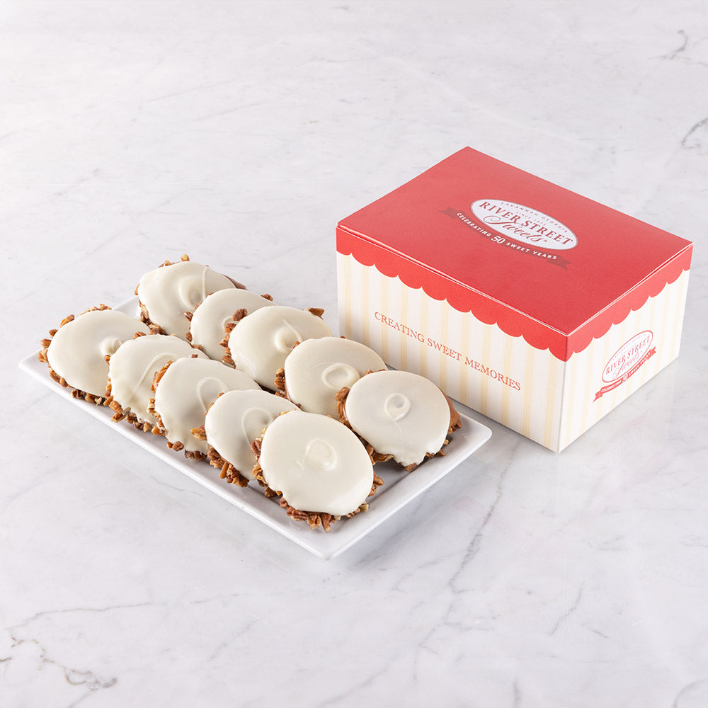 A box of white chocolate bear claws cookies next to a plate with bear claws on it, placed on a marble surface.
