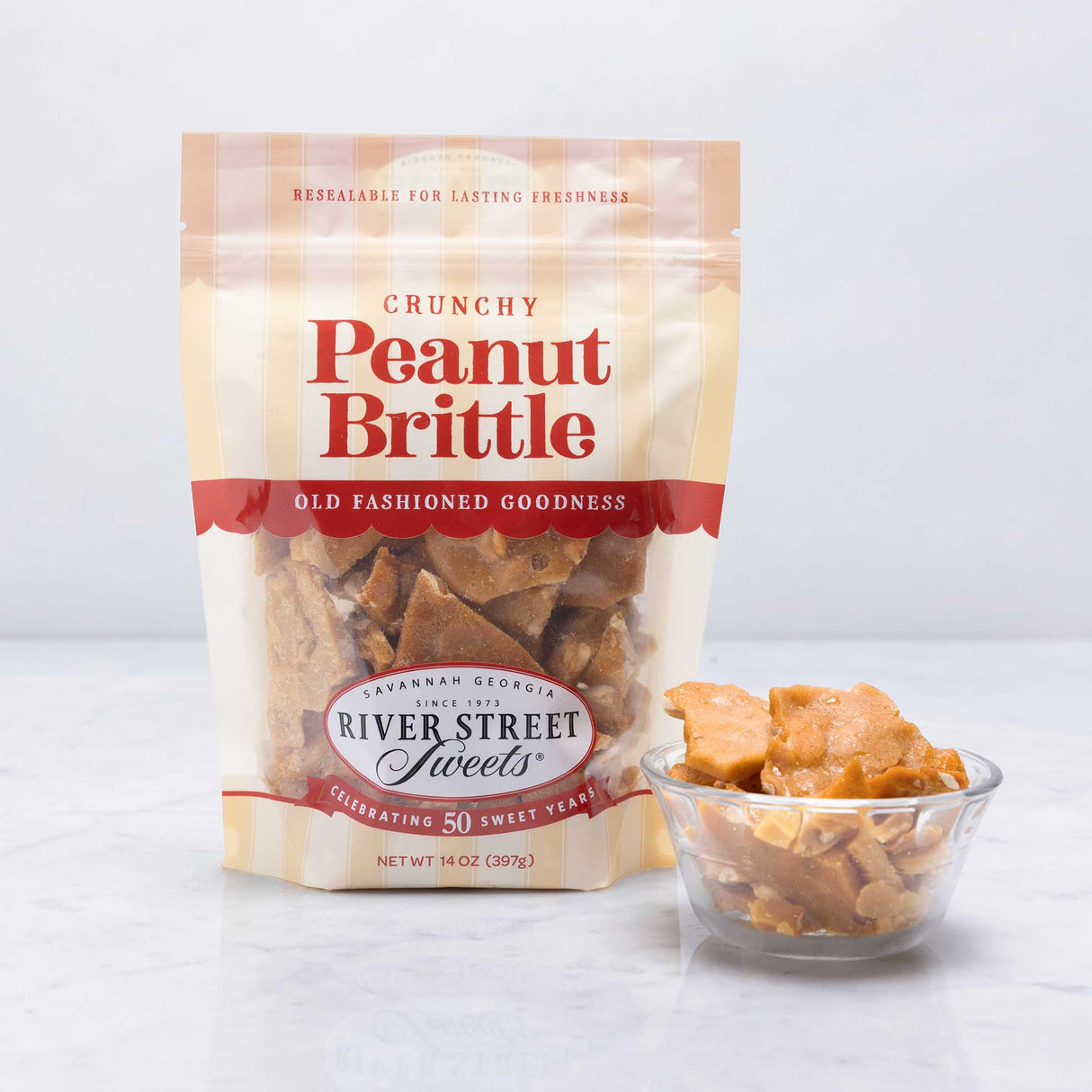 A resealable pouch of Peanut Brittle candy displayed alongside a clear bowl filled with peanut brittle pieces.