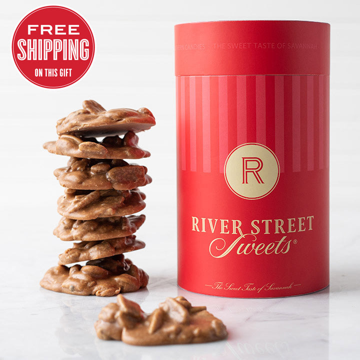 A red cylindrical candy canister labeled 'River Street Sweets' with a stack of praline candies in front of it,