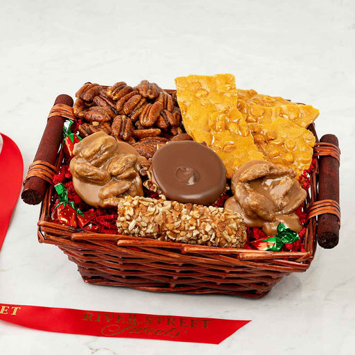 Basket of assorted snacks including nuts and candies on a white surface with a River Street Treats ribbon.
