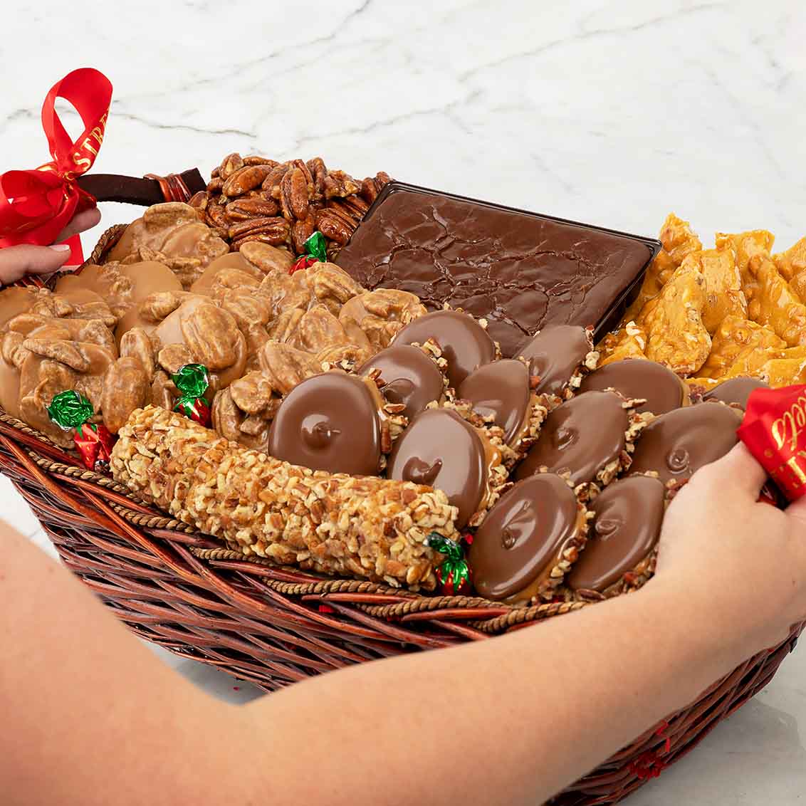 Basket of assorted snacks including pralines, chocolate, and nuts on a white surface.