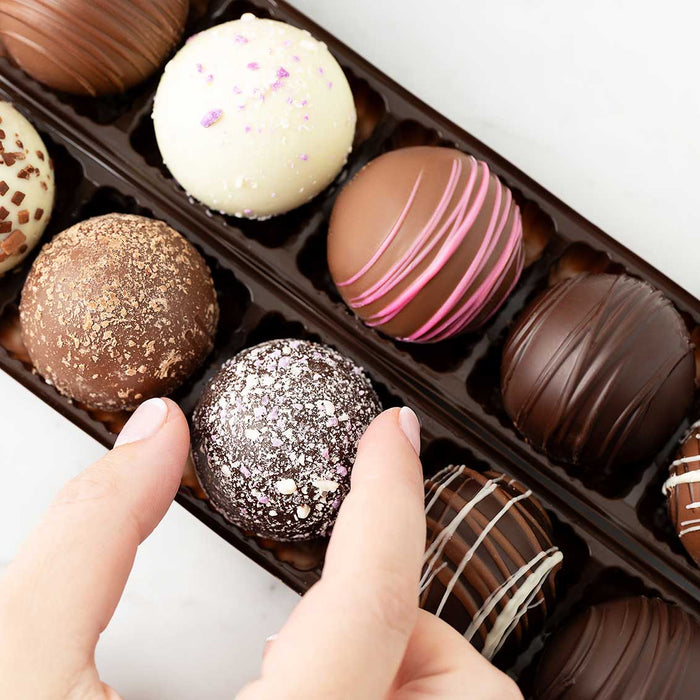 Assorted chocolate truffles in a box with a hand reaching for one.