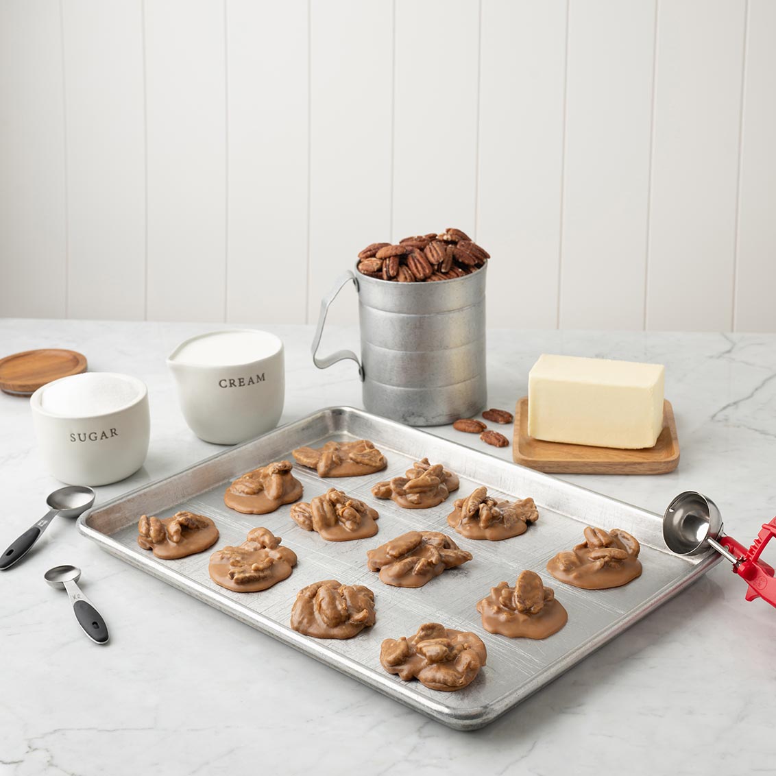 Baking tray with pralines, measuring cups, and ingredients on a marble countertop.