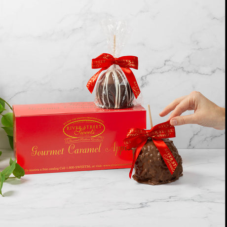 Gourmet caramel apple with red ribbon packaging on a marble surface