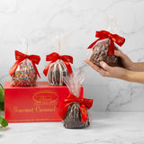 Gourmet caramel apples with red bows in front of a River Street Sweets box on a marble surface.