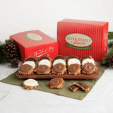 A gift set of River Street Sweets holiday treats, featuring assorted bear claws on a wooden board, with two red branded gift boxes and pine decorations on a white marble surface.