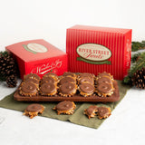 River Street Sweets chocolate bear claws displayed on a wooden tray with two red branded gift boxes, pinecones, and greenery on a light neutral background.