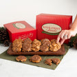 A hand reaches for a pralinefrom a wooden board, with red River Street Sweets boxes and pinecones in the background.