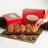 A hand reaches for a pralinefrom a wooden board, with red River Street Sweets boxes and pinecones in the background.
