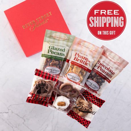 An assortment of individually wrapped chocolate and nut treats in a red gift box with a label stating 'Free Shipping on this Gift'. The treats appear to include glazed pecans, chocolate peanuts, pecan divinity, chocolate pretzel, a praline, a bear claw, and peanut brittle.