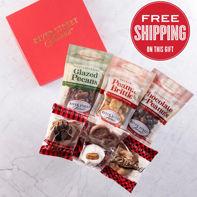 An assortment of individually wrapped chocolate and nut treats in a red gift box with a label stating 'Free Shipping on this Gift'. The treats appear to include glazed pecans, chocolate peanuts, pecan divinity, chocolate pretzel, a praline, a bear claw, and peanut brittle.