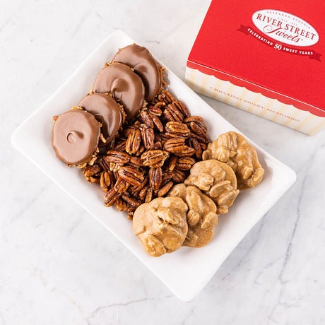 A gift box of assorted chocolates which includes pralines, bear claws, and glazed pecans presented on a white plate with the box partially visible in the top right corner.