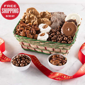 A festive Christmas basket containing an assortment of sweet treats including pralines, divinity, chocolate almond toffee, assorted chocolate bear claws, glazed pecans, and chocolate covered peanuts. The basket is adorned with red and green holiday accents, and there is a red ribbon in the foreground.
