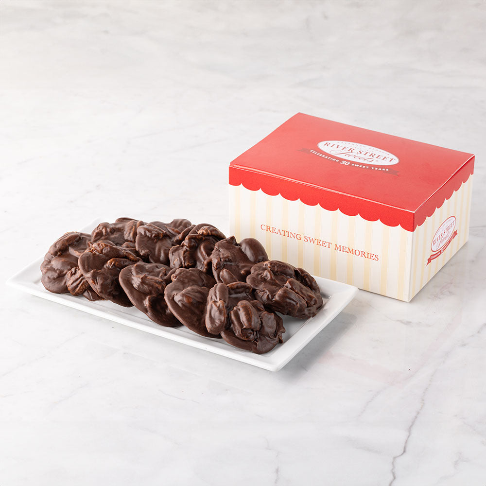 A box of chocolate pralines with the lid open, displaying multiple chocolate candies on a white plate.
