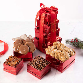 A gift tower box containing various sweet treats such as chocolate covered nuts and pralines, arranged in red boxes with a red ribbon.