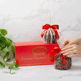 Hands unwrapping an apple with a red box and plant in the background