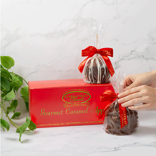 Hands unwrapping an apple with a red box and plant in the background