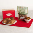 River Street Sweets gift set featuring a red box of pralines and bear claws, a bag of glazed pecans, and a small bowl of pecans arranged on a red cloth over a white marble surface.