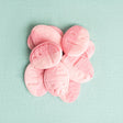 A pile of light pink oval-shaped buttons with a subtle embossed pattern, arranged on a textured mint green background.