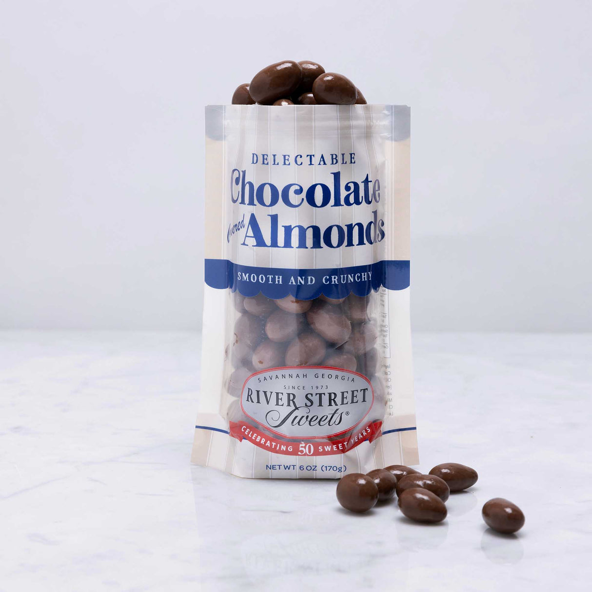 A clear plastic bag with a label displaying chocolate covered almonds, with a few almonds scattered in front.