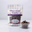 A packaged bag of River Street Sweets Chocolate Covered Cashews with a transparent section showing the cashews inside. There is also a small bowl of chocolate covered cashews beside the bag.