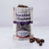 A clear plastic bag with a label displaying chocolate covered cashews. Some chocolate cashews are scattered in front of the bag.