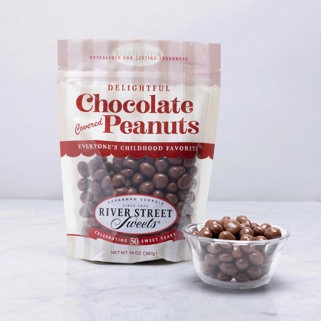 A resealable pouch of Chocolate Covered Peanuts branded as River Street Sweets, with a transparent section showing the chocolate-covered peanuts inside.