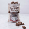 A clear plastic bag filled with chocolate covered pecans, with a label that reads 'Scrumptious Chocolate Pecans' and the brand 'River Street Sweets'.