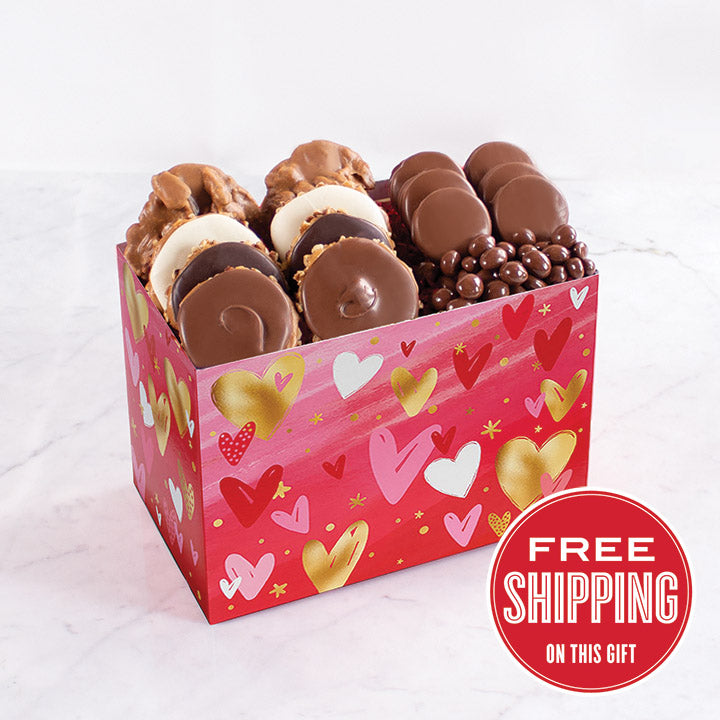 A box of various chocolate confections, including pralines, chocolate-dipped oreos, and peanuts, presented in a box decorated with hearts and love-themed patterns.