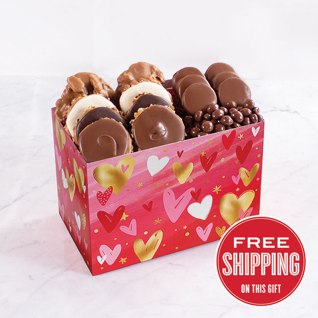 A box of various chocolate confections, including pralines, chocolate-dipped oreos, and peanuts, presented in a box decorated with hearts and love-themed patterns.
