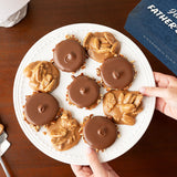 Plate of chocolate bear claws and pralines with a hand reaching for one, on a wooden surface with a Father's Day box in the background