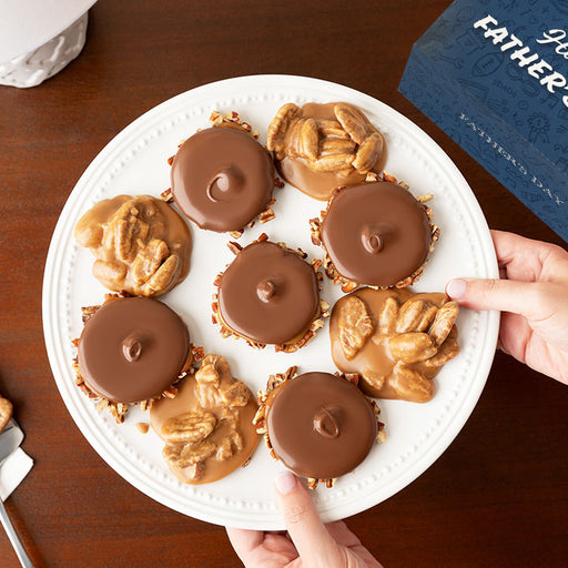 Plate of chocolate bear claws and pralines with a hand reaching for one, on a wooden surface with a Father's Day box in the background