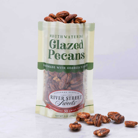 A clear plastic bag with a green label that reads 'Glazed Pecans'. The bag is filled with pecan nuts and has a white ribbon decoration.
