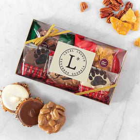A clear gift box containing an assortment of chocolate bear claws and glazed nuts, tied with a red ribbon. A few pieces are placed outside of the box, and the brand's logo is visible on a tag within the box.