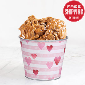 A bucket of heart-patterned, filled with pralines, on a marble surface with a 'Free Shipping' label in the top right corner.