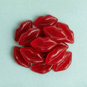 A pile of glossy red lip-shaped candies or beads on a light aqua textured fabric background.