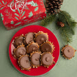 Holiday-themed product photo showing a red plate filled with bear claws, with a red gift box and pine branches in the background.