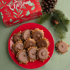 Holiday-themed product photo showing a red plate filled with bear claws, with a red gift box and pine branches in the background.