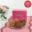 Plate of pralines, glazed pecans, bear claws with a 'Happy Mother's Day' gift box and flowers on a pink surface.
