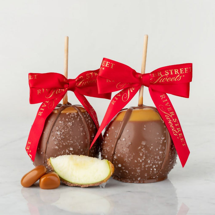 Two chocolate-dipped apples with red ribbons on a light gray background