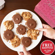 Bear claws and pralines on a white plate with a hand reaching for one, and a pink box in the background.