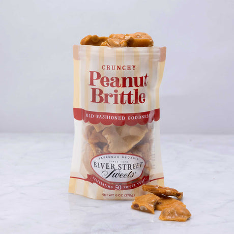 A clear plastic bag with a label reading 'Crunchy Peanut Brittle', filled with peanut brittle candies.
