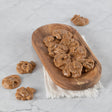 Bite-sized pralines arranged on a wooden plate with a few pieces scattered on a marble surface.