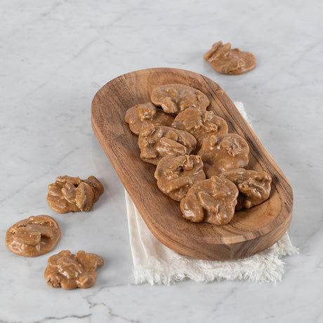 Bite-sized pralines arranged on a wooden plate with a few pieces scattered on a marble surface.