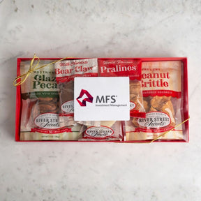 A gift box of gourmet snacks and sweets arranged in a red tray, tied with a gold string and covered with a white card. Visible packaged items include Chocolate Bear Claw, World Famous Pralines, Peanut Butter Brittle, and River Street Sweets.