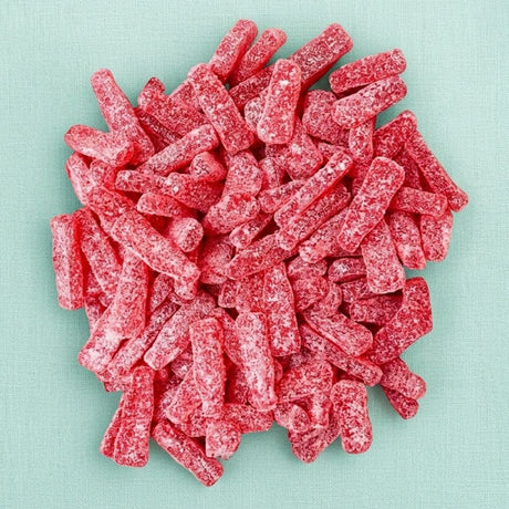 A pile of red, sugar-coated, cylindrical candy sticks, resembling sour gummy strips, arranged on a light mint green textured background.