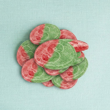 A pile of oval, sugar-coated candies in alternating red and green sections, arranged on a light aqua textured background.