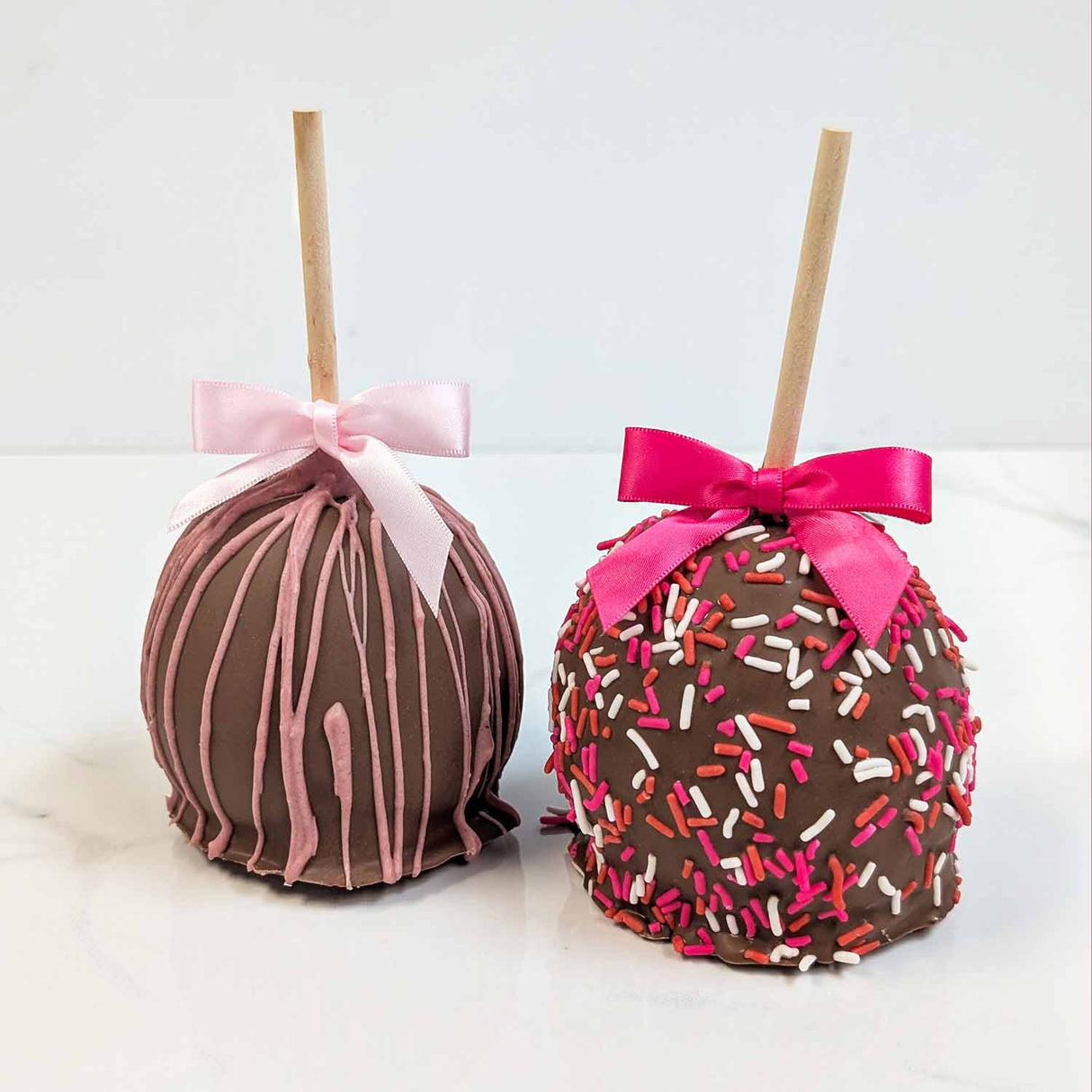 Two decorated apples with pink and white bows on a white background