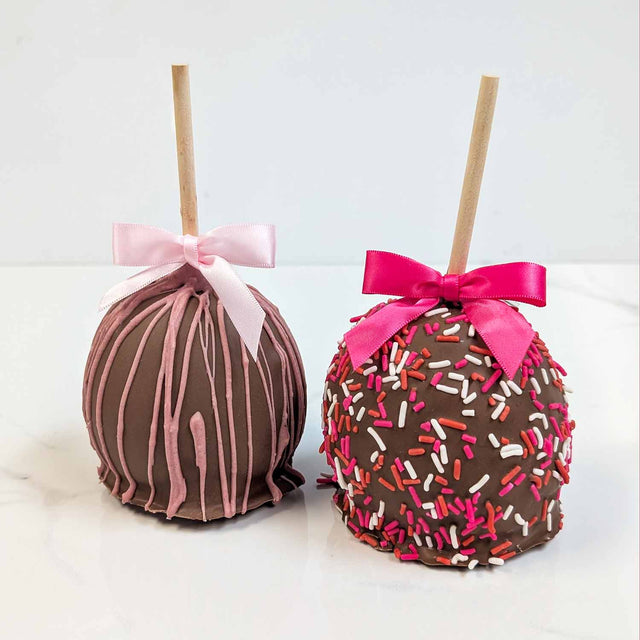 Two decorated apples with pink and white bows on a white background